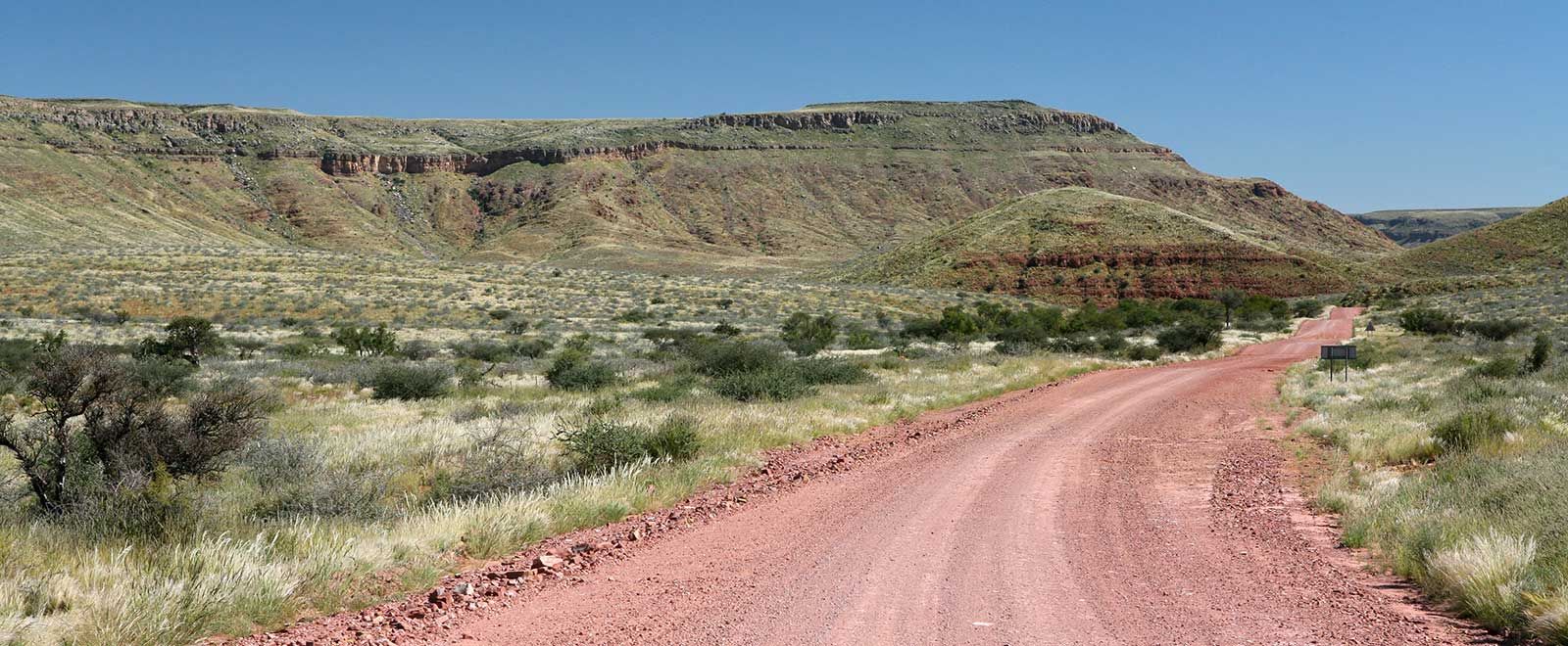 Red gravel road leading towards flat-topped hills near Grünau